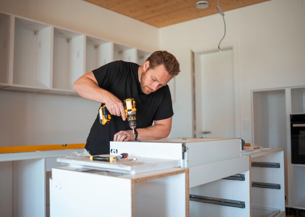 Focused mid adult Caucasian man uses a cordless drill to assemble a kitchen cabinet, demonstrating skill in home improvement and interior design.