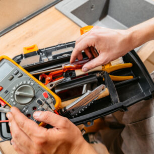 Mid-adult electrician searching for a tool in a tool box before fixing something in an apartment. Close-up.